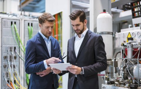 Two businessmen in factory looking at tablet