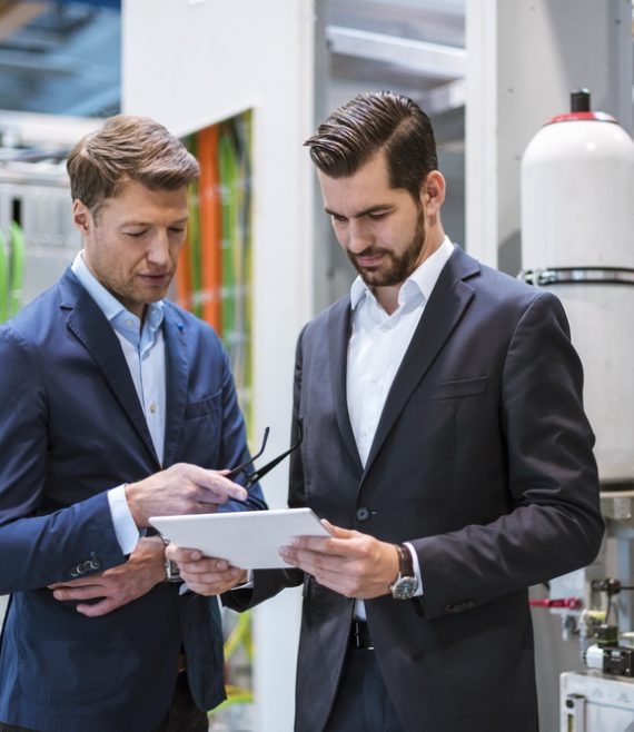 Two businessmen in factory looking at tablet
